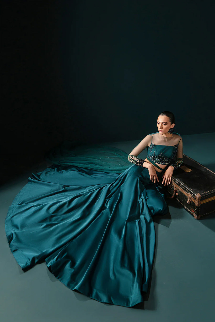 Model in a seated top shot wearing sea green formal lehenga choli with net drape attached