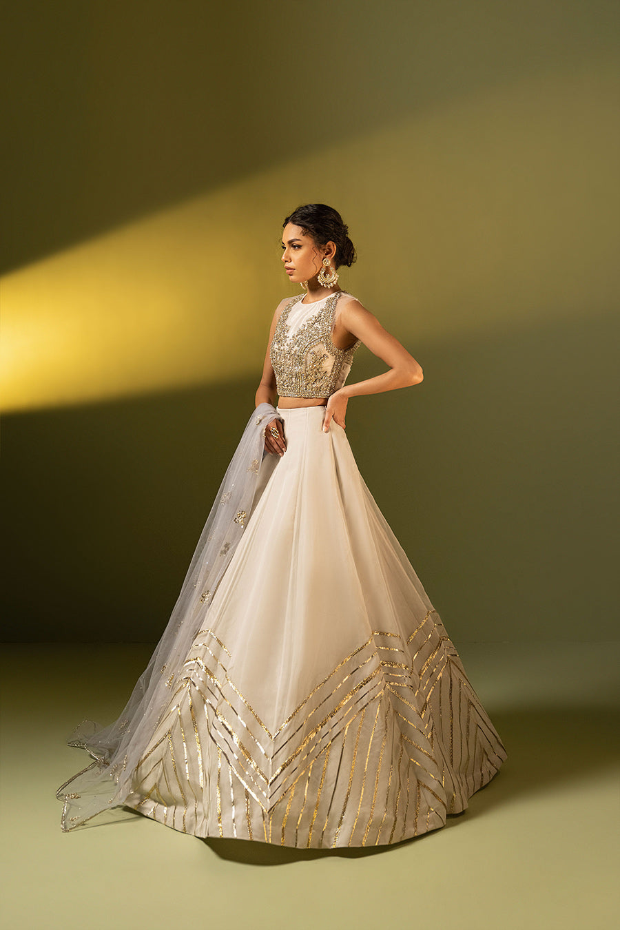 Model in side shot wearing ivory choli paired with net dupatta and organza lehenga