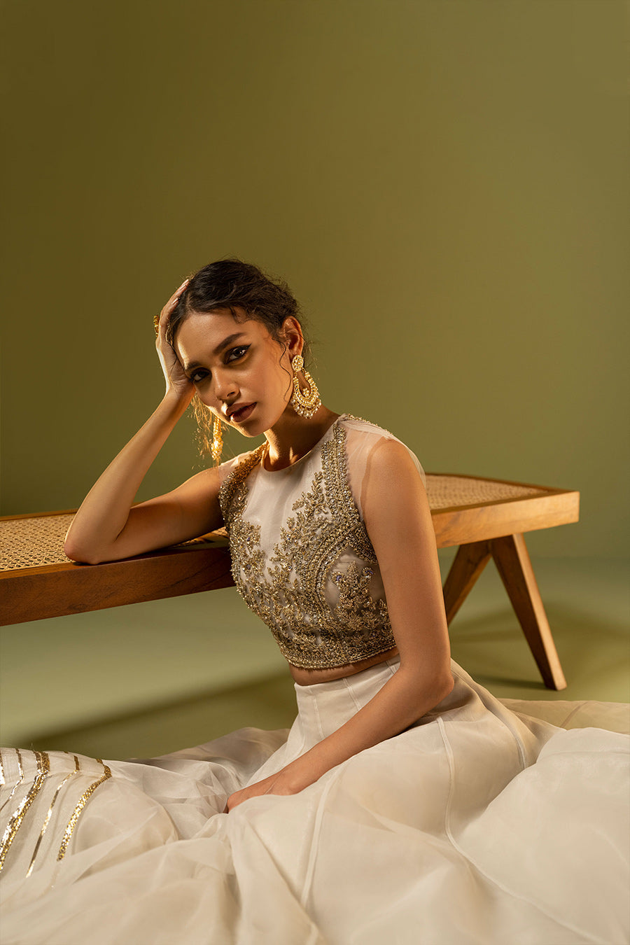 Model in seated closeup shot wearing ivory choli paired with organza lehenga