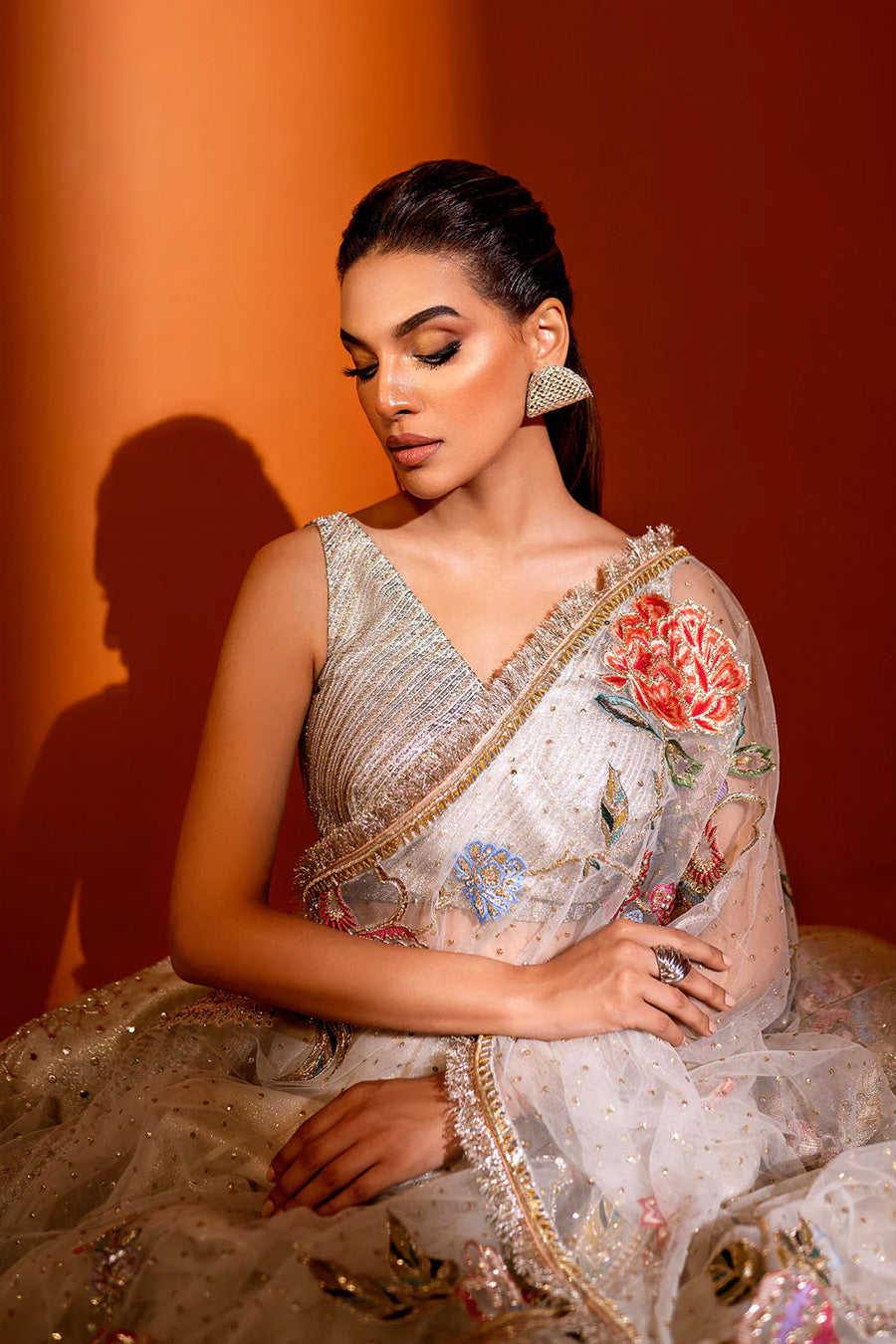 model in a seated shot wearing ivory net dupatta paired with a hand-embellished organza lehenga and a silk brocade blouse