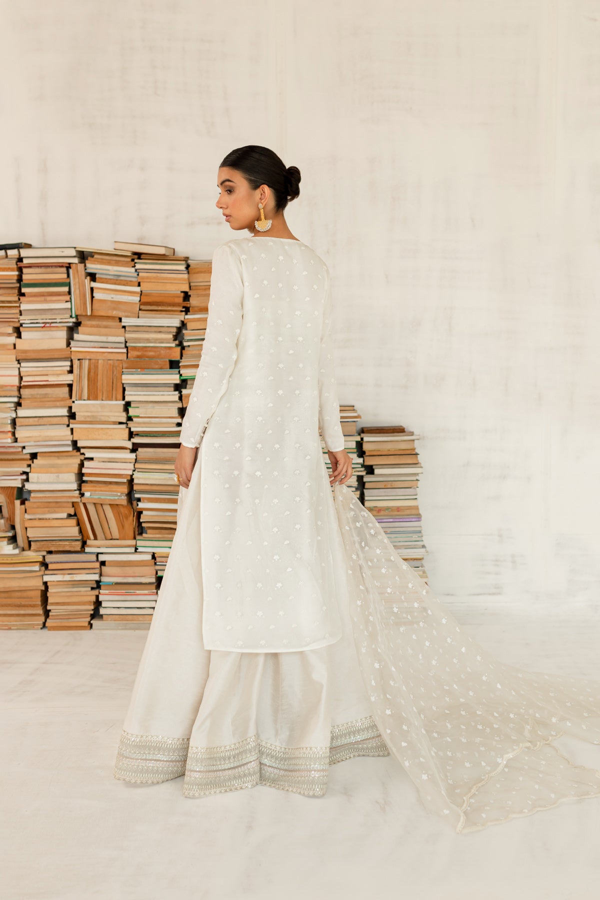 Model in a back view shot wearing an ivory organza shirt paired with an organza dupatta and a silk katan sharara