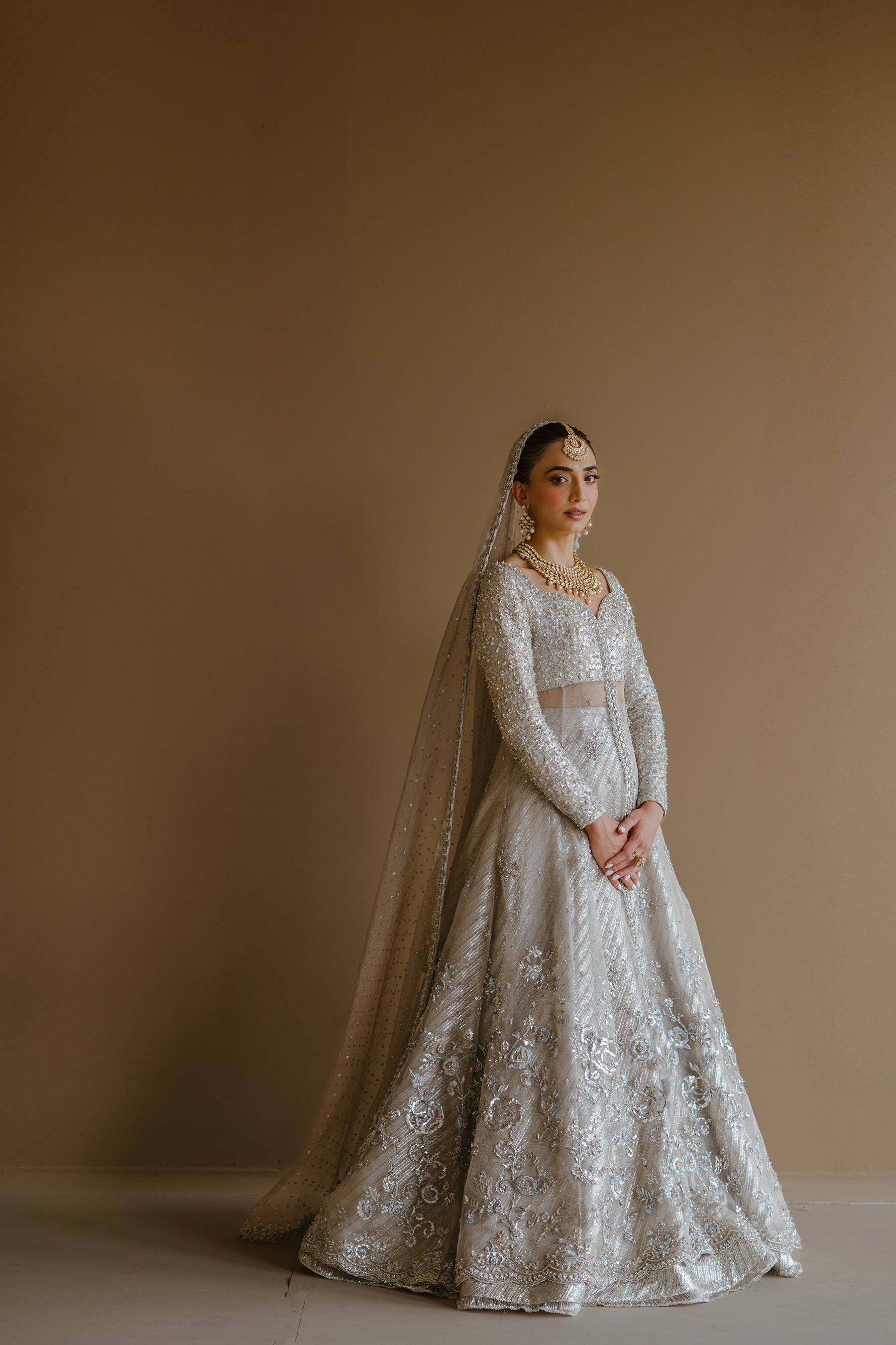 Model in a full side shot wearing silver peshwas paired with a metallic lehenga completed with a Zari net dupatta