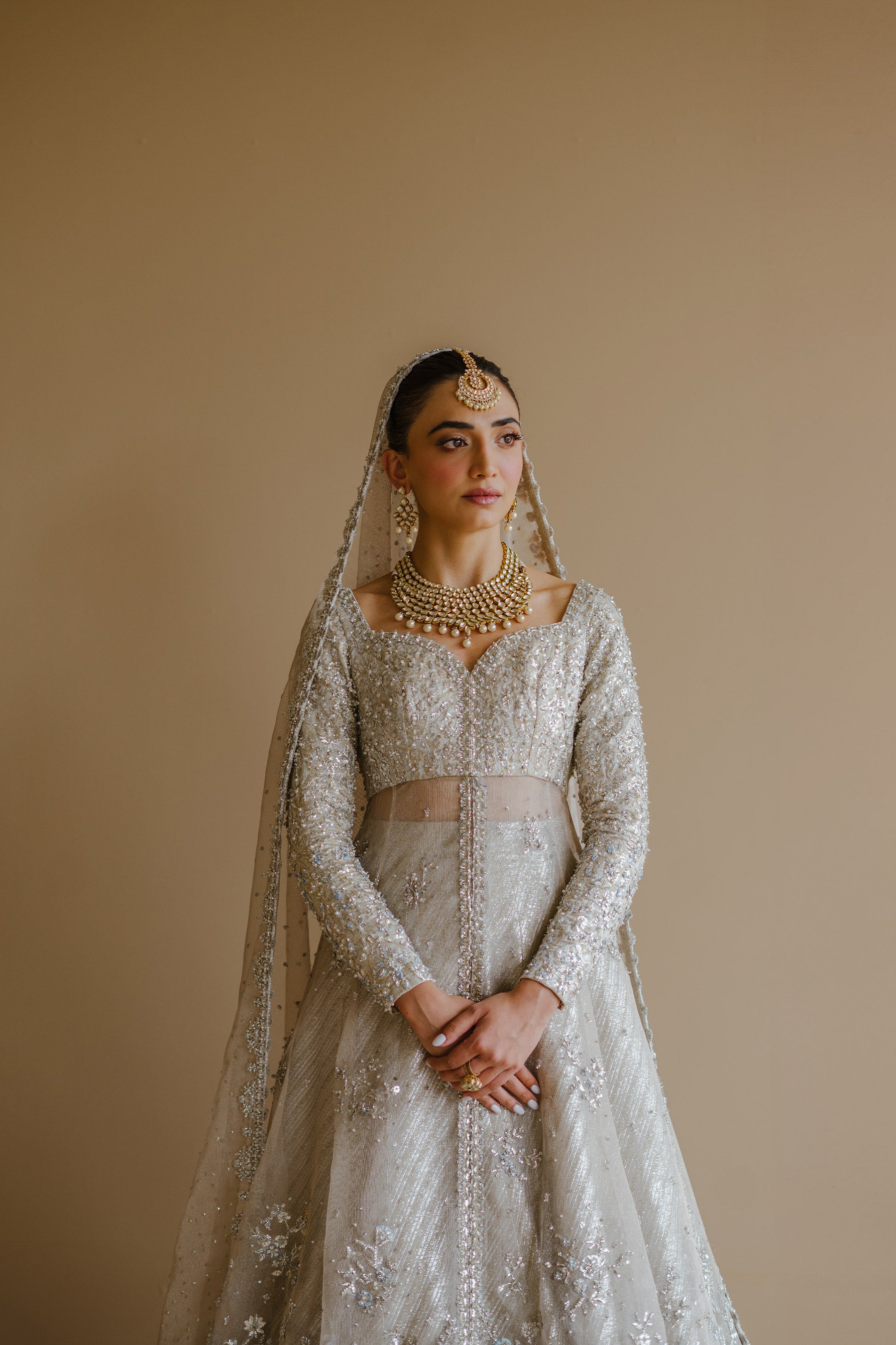 Model in a front half closeup shot wearing silver peshwas paired with a metallic lehenga completed with a Zari net dupatta