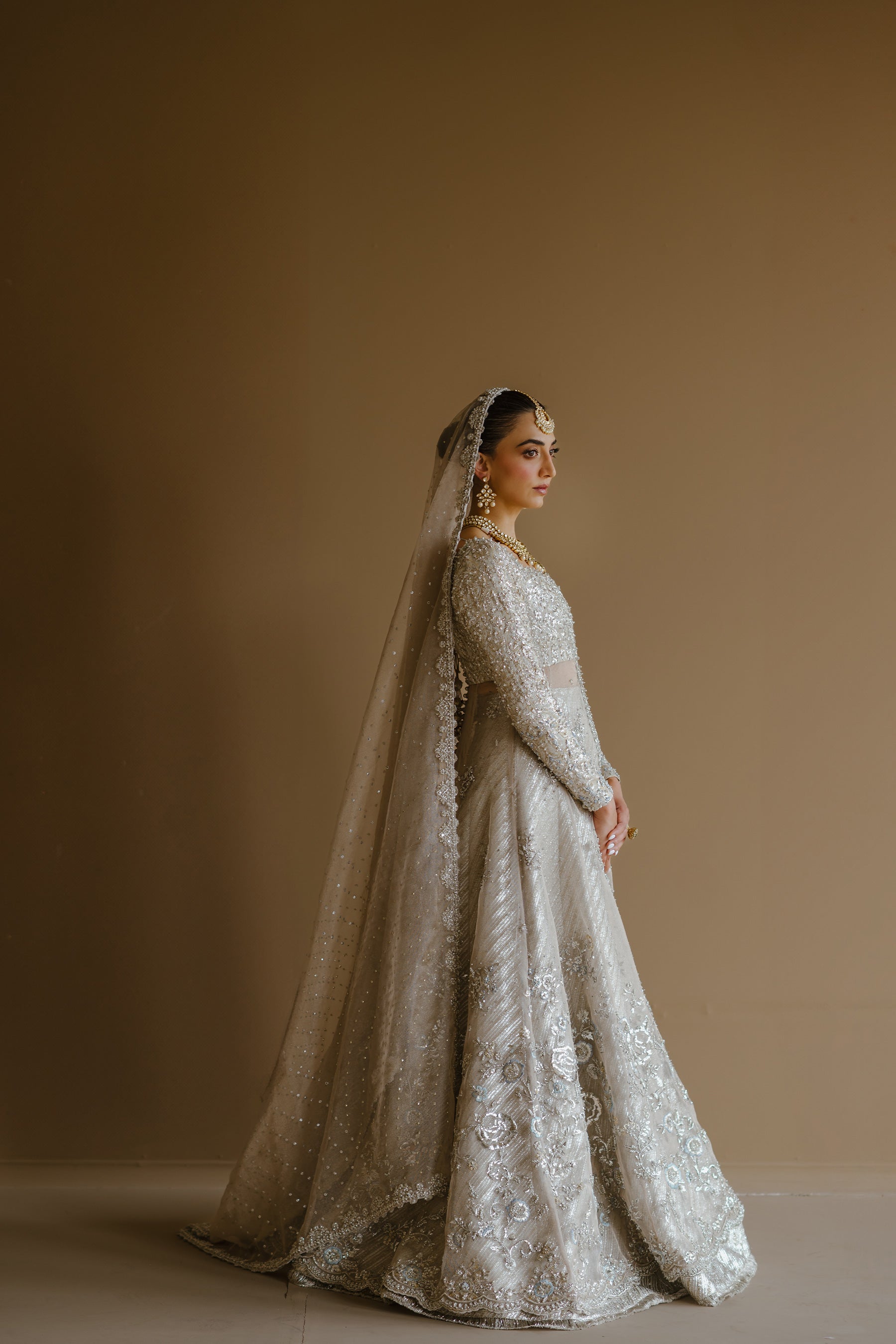 Model in a full side shot wearing silver peshwas paired with a metallic lehenga completed with a Zari net dupatta