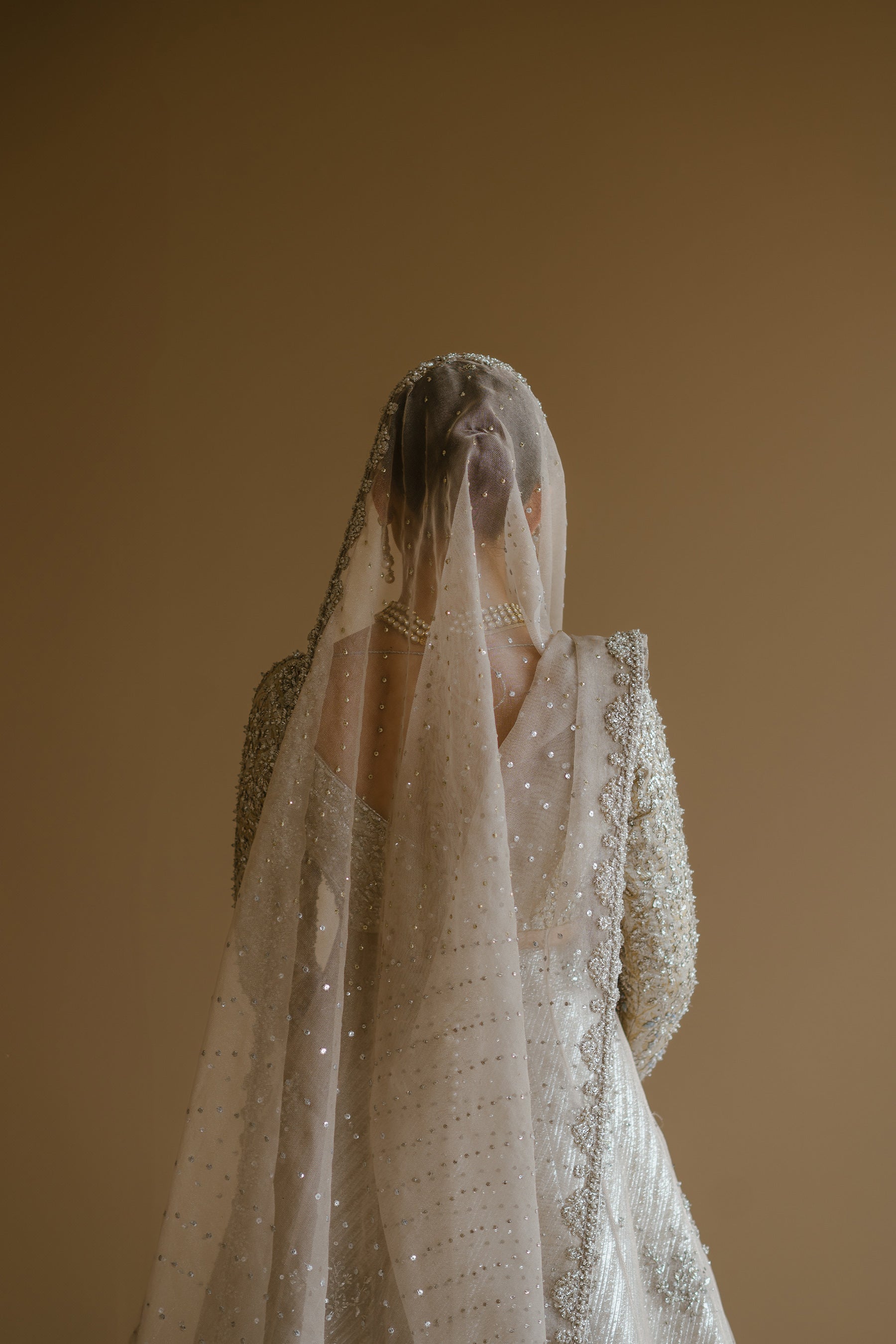 Model in a back shot wearing silver peshwas paired with a metallic lehenga completed with a Zari net dupatta