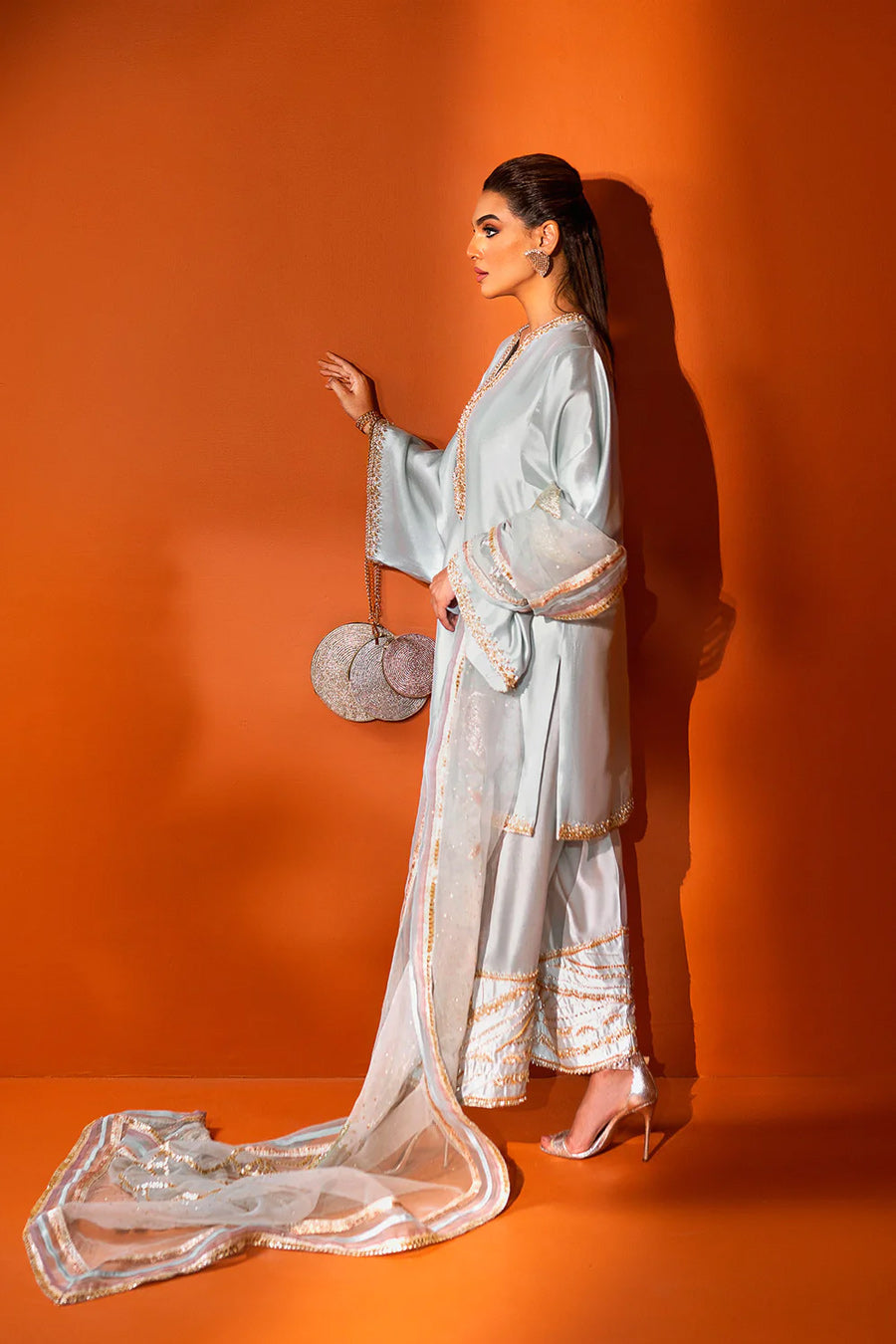 model in a side shot wearing a formal light blue shalwar-kurta ensemble made in silk with the shalwar paired with an organza dupatta