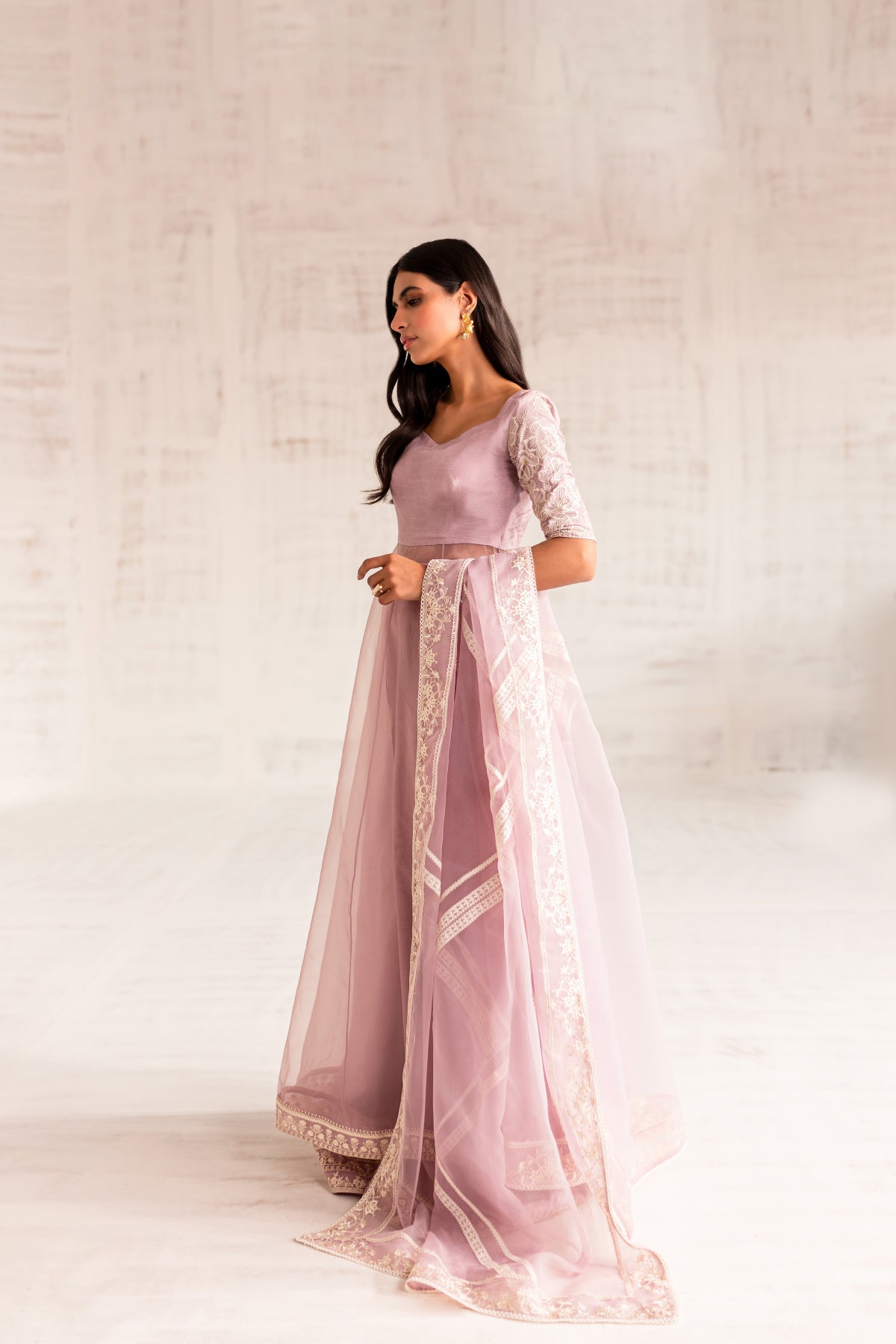 Model in a side view shot wearing an organza light pink long flared pishwas paired with an organza dupatta and silk katan trousers