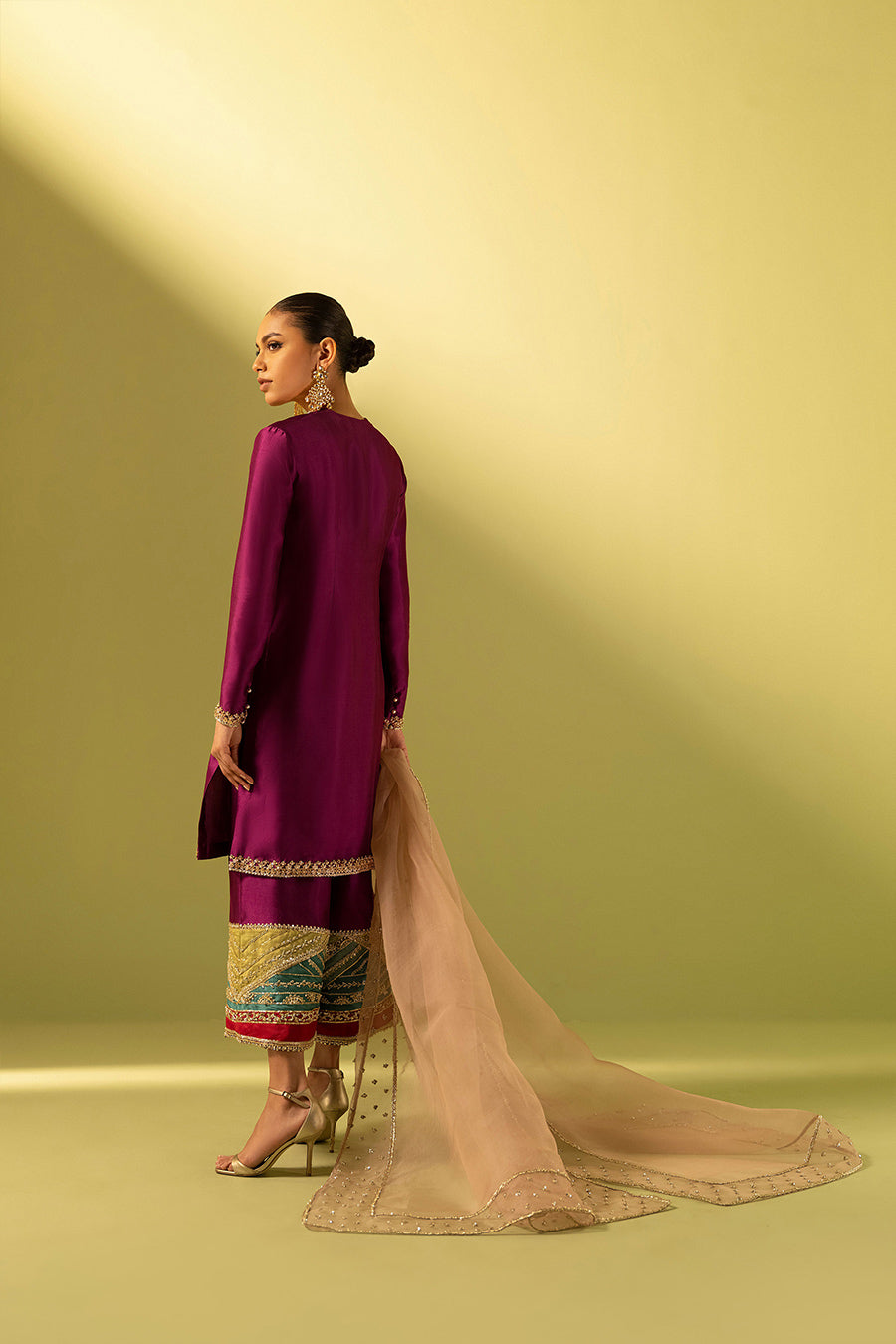 Model in a back shot wearing a magenta tissue raw silk culottes kurta paired with an embellished light pink organza dupatta