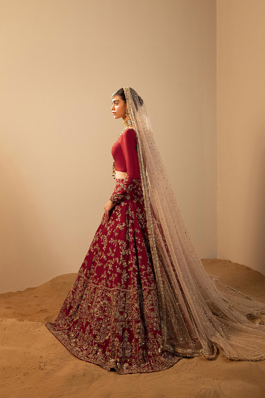 Model in a side shot wearing maroon raw silk lehenga choli paired with silk dupatta and net veil 