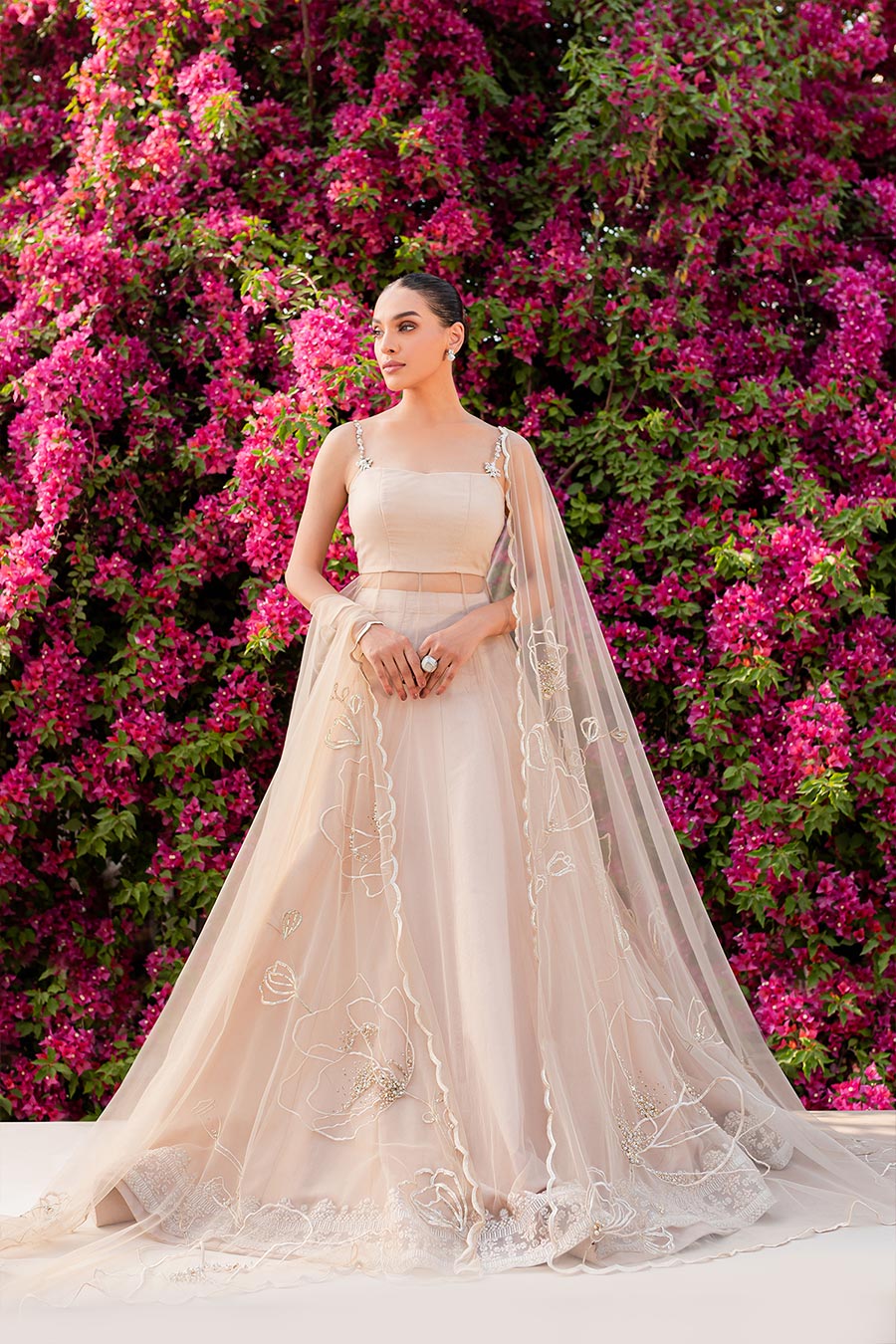 model in a front shot wearing a formal nude pink flared net shirt paired with dupatta and a lehenga