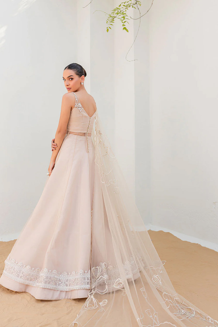 model in a side shot wearing a formal nude pink flared net shirt paired with dupatta and a lehenga