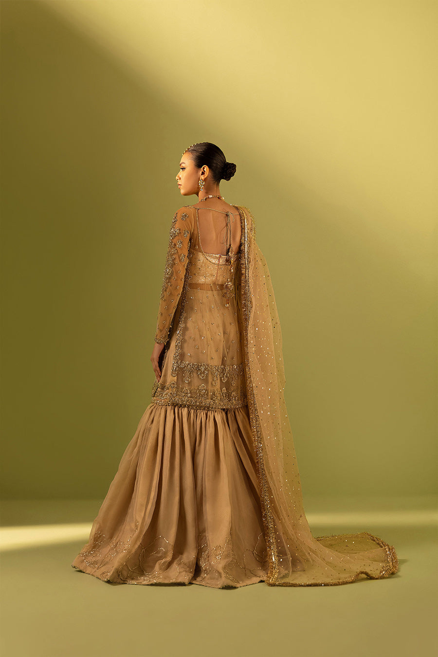 Model in a back shot wearing nude pink organza shirt paired with gharara and net dupatta 