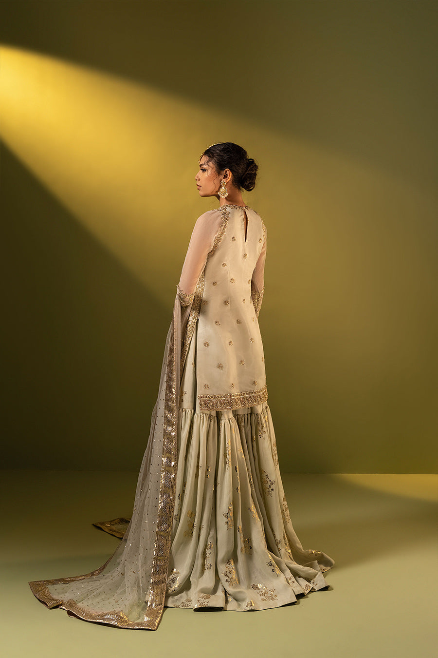 Model in a back side shot wearing formal pistachio organza shirt paired with a silk chiffon gharara and a net dupatta 