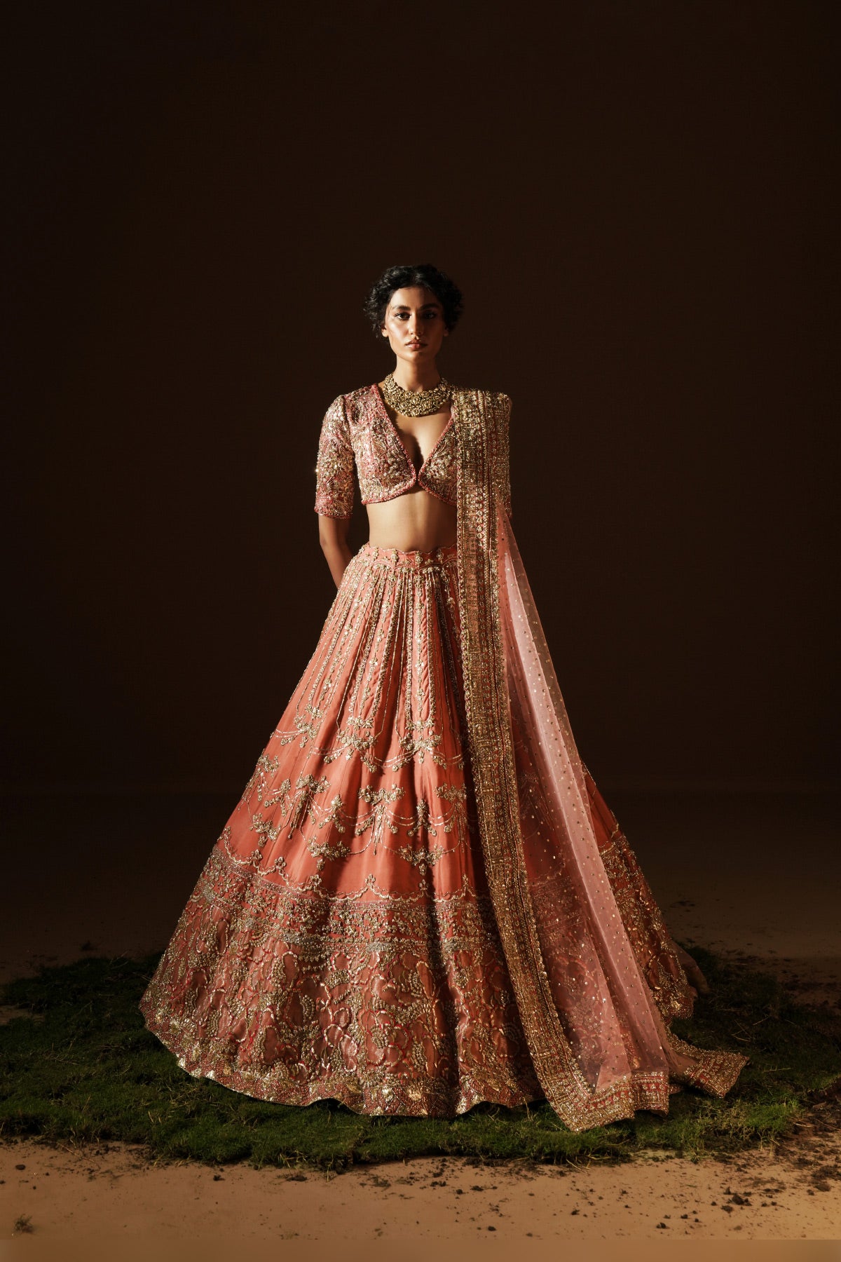 Model in a front view angle wearing a warm coral handcrafted raw silk lehenga choli paired with a net dupatta