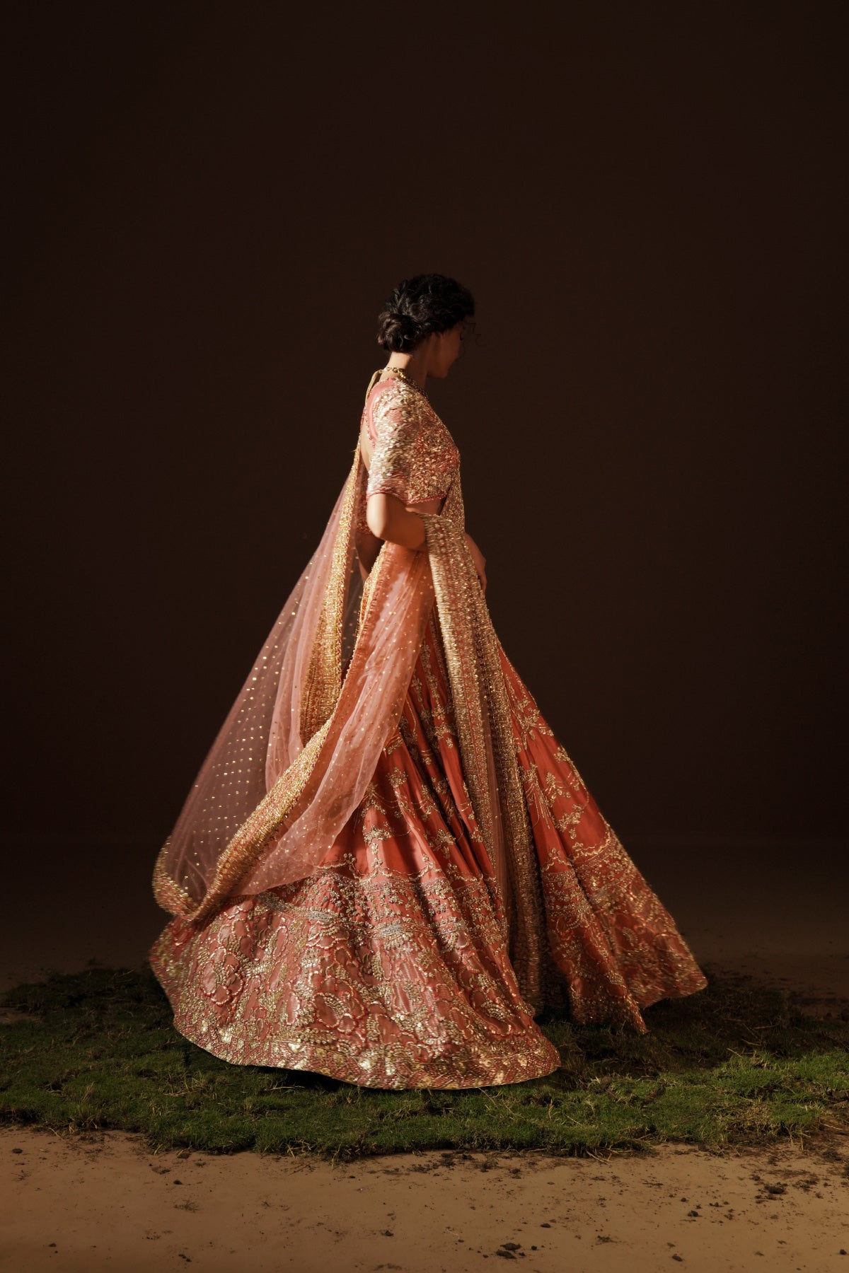 Model in a side view angle wearing a warm coral handcrafted raw silk lehenga choli paired with a net dupatta