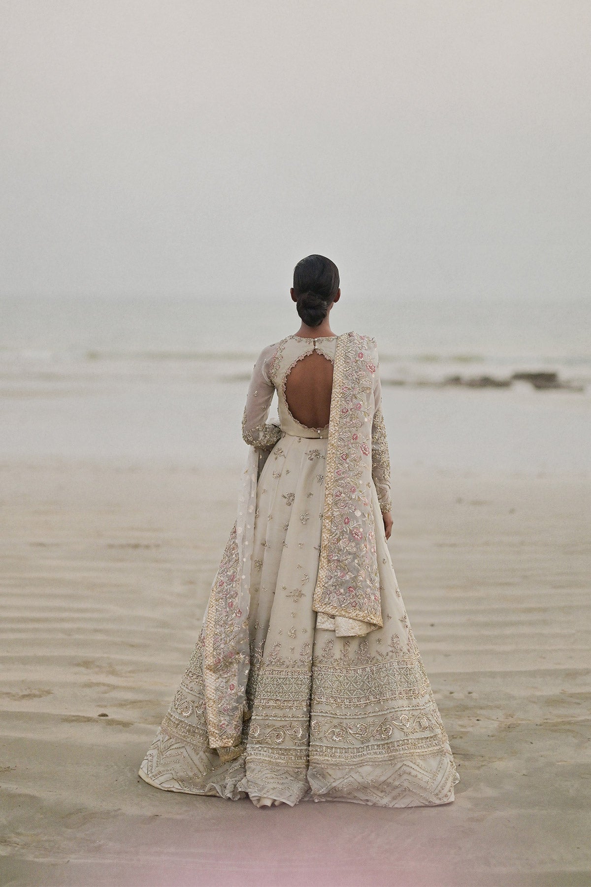 Model in a back shot wearing long pishwas gown in organza silk paired with an organza zari dupatta and organza lehenga 