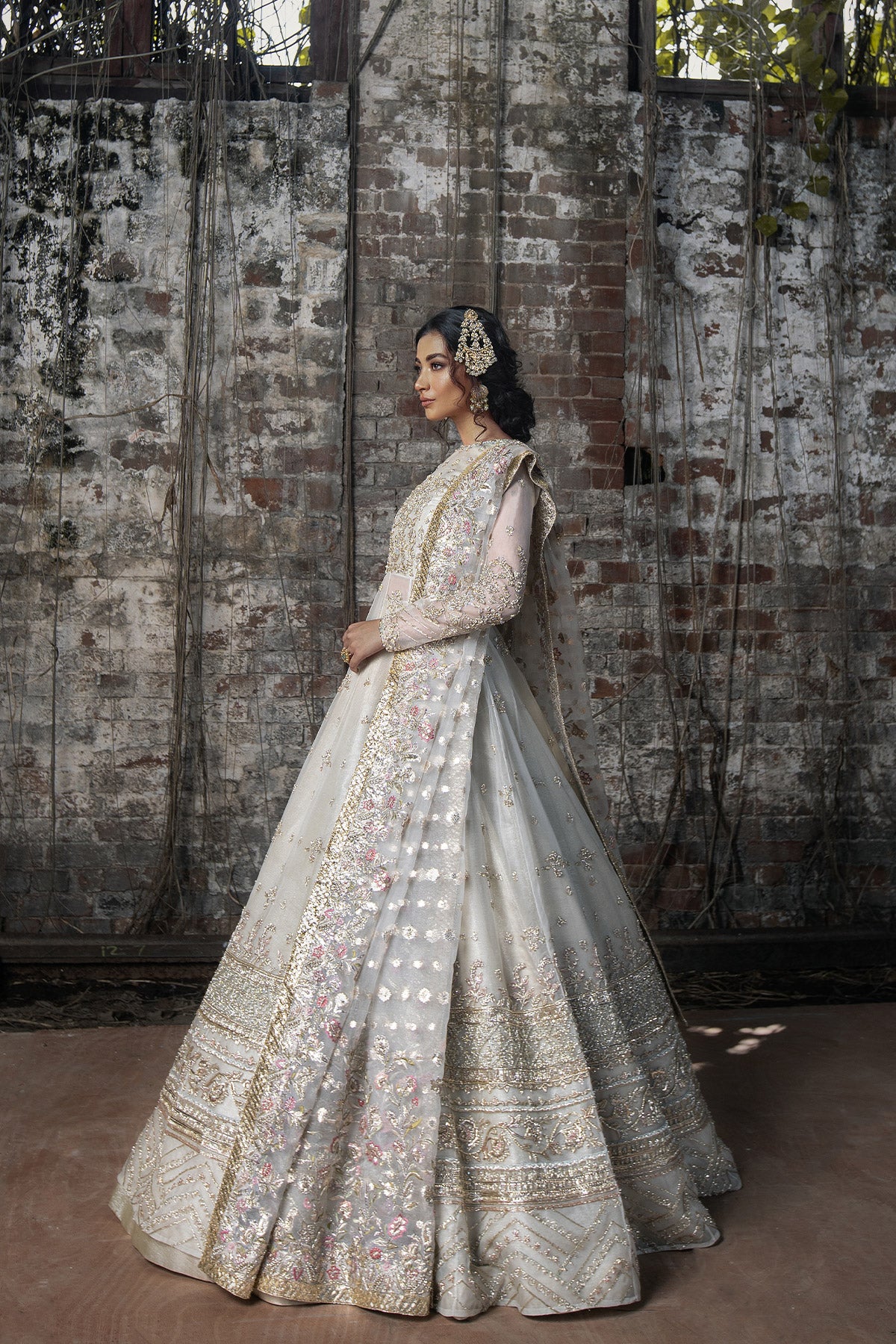 Model in a side view shot wearing long pishwas gown in organza silk paired with an organza zari dupatta and organza lehenga 