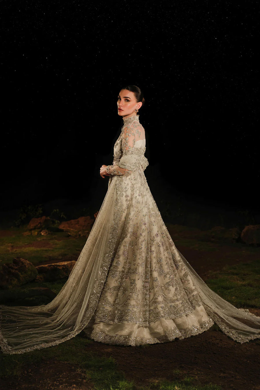 Model in a side shot wearing a white bridal pishwas with organza lehenga and long flowing drapes attached to the back