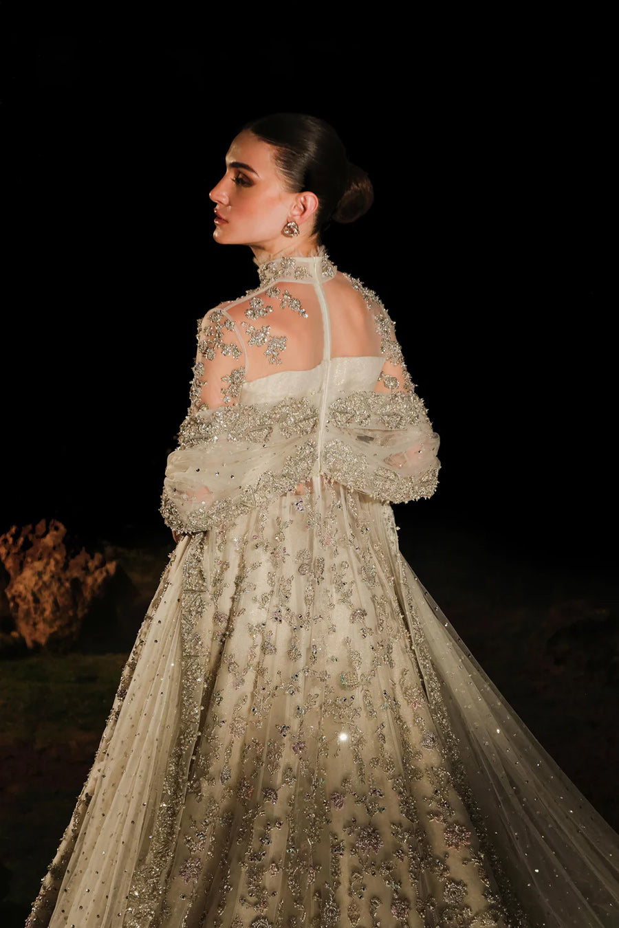 Model in a back shot wearing a white bridal pishwas with organza lehenga and long flowing drapes attached to the back