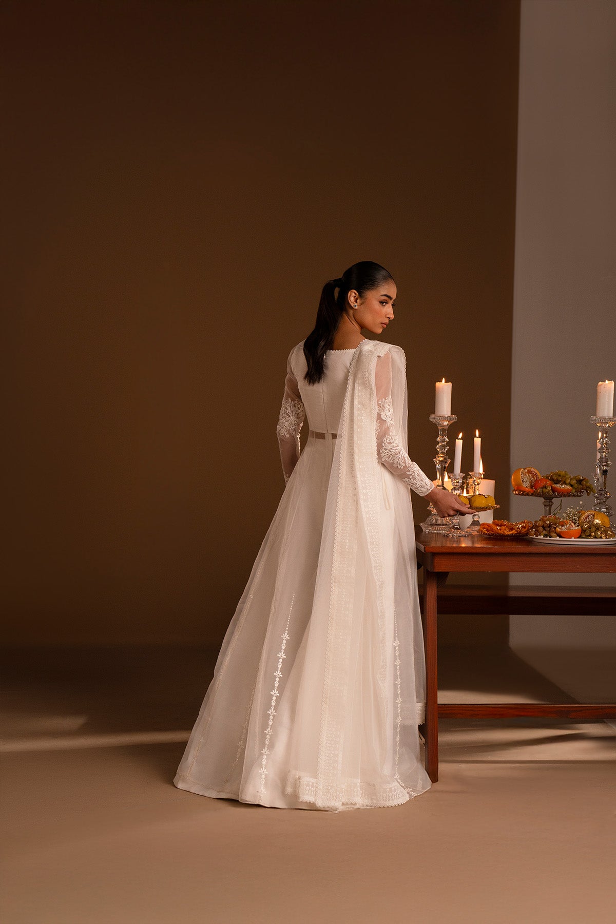 Model in a back shot wearing a long flared pishwas with embroidered shirt and organza dupatta. 