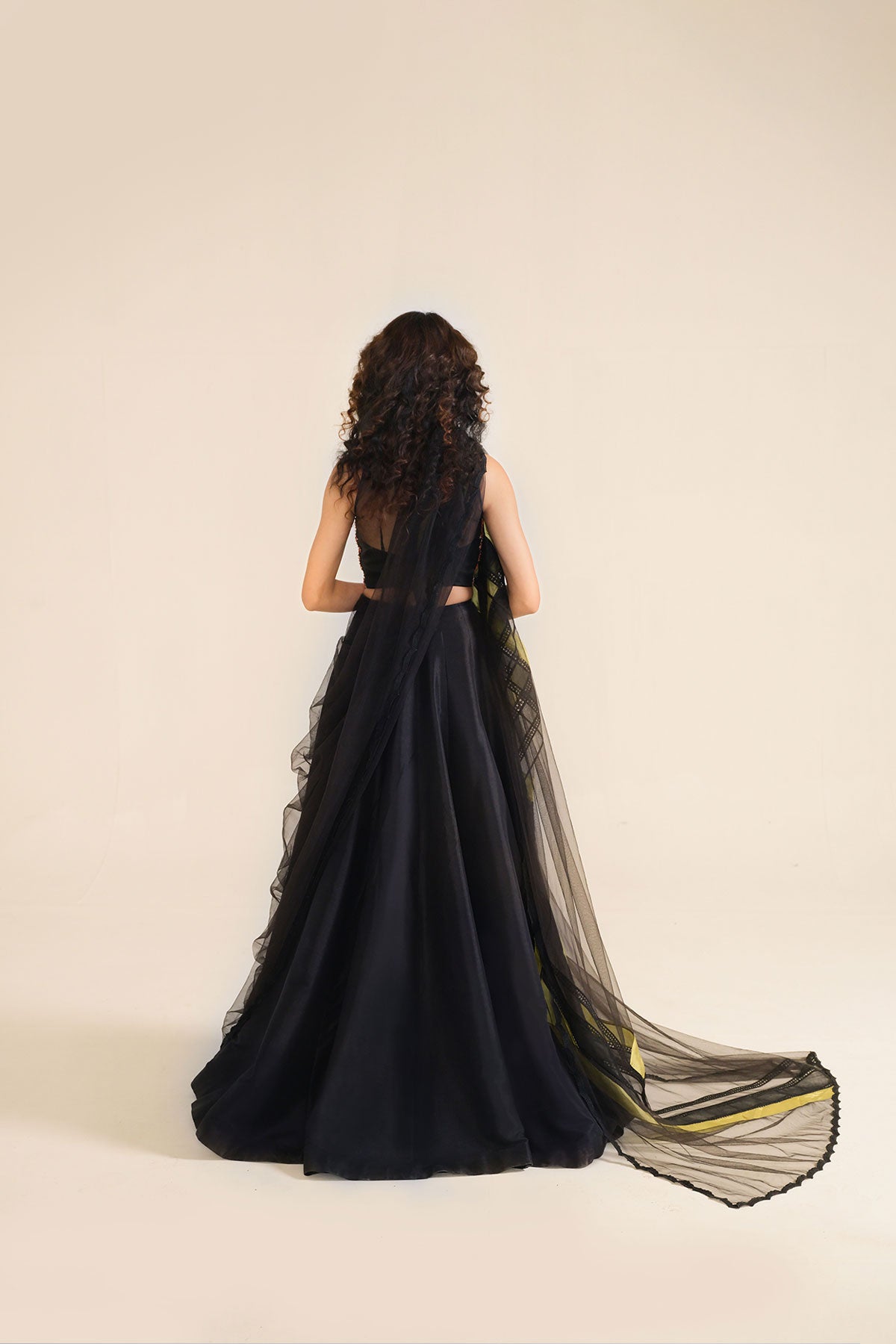 Model in a back shot wearing black formal lehenga saree paired with lehenga and a net saree drape