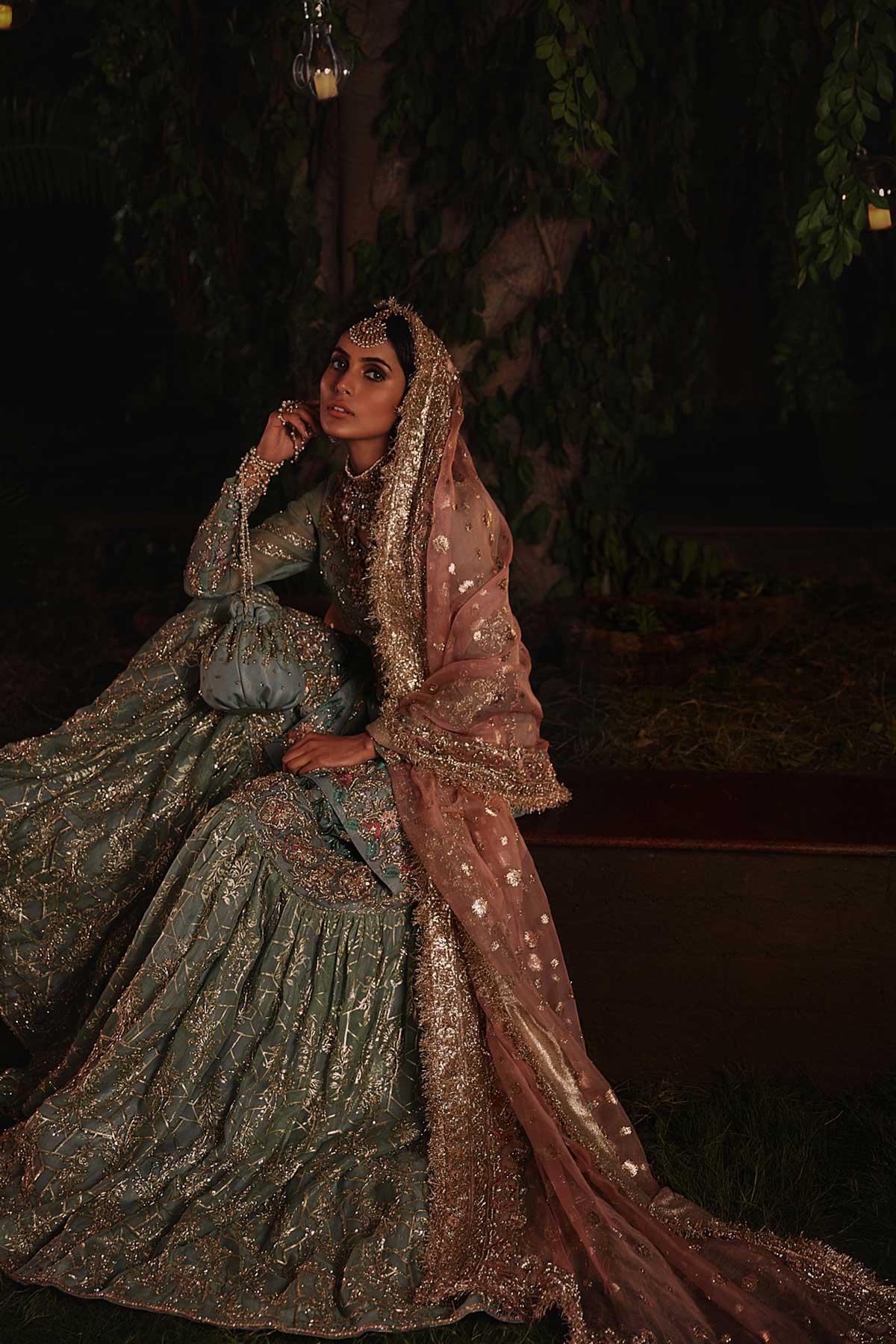 model in a seated shot wearing straight silk organza shirt in dusty blue color paired with silk organza gharara and organza zari dupatta 