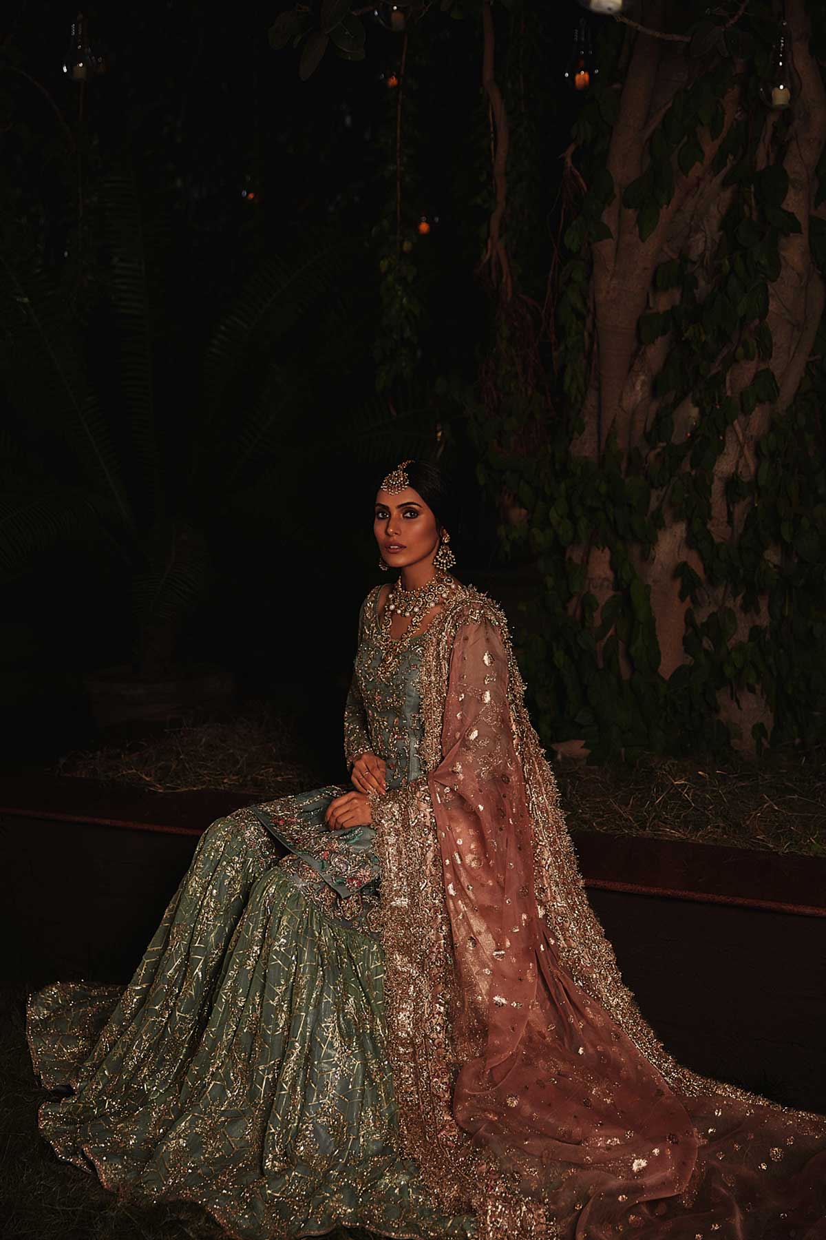 model in a seated shot wearing straight silk organza shirt in dusty blue color paired with silk organza gharara and organza zari dupatta 