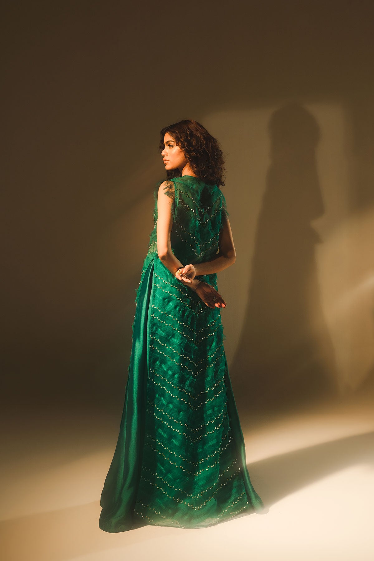 Model in a back shot wearing a emerald green silk organza front-open jacket paired with a bustier and tissue silk pants