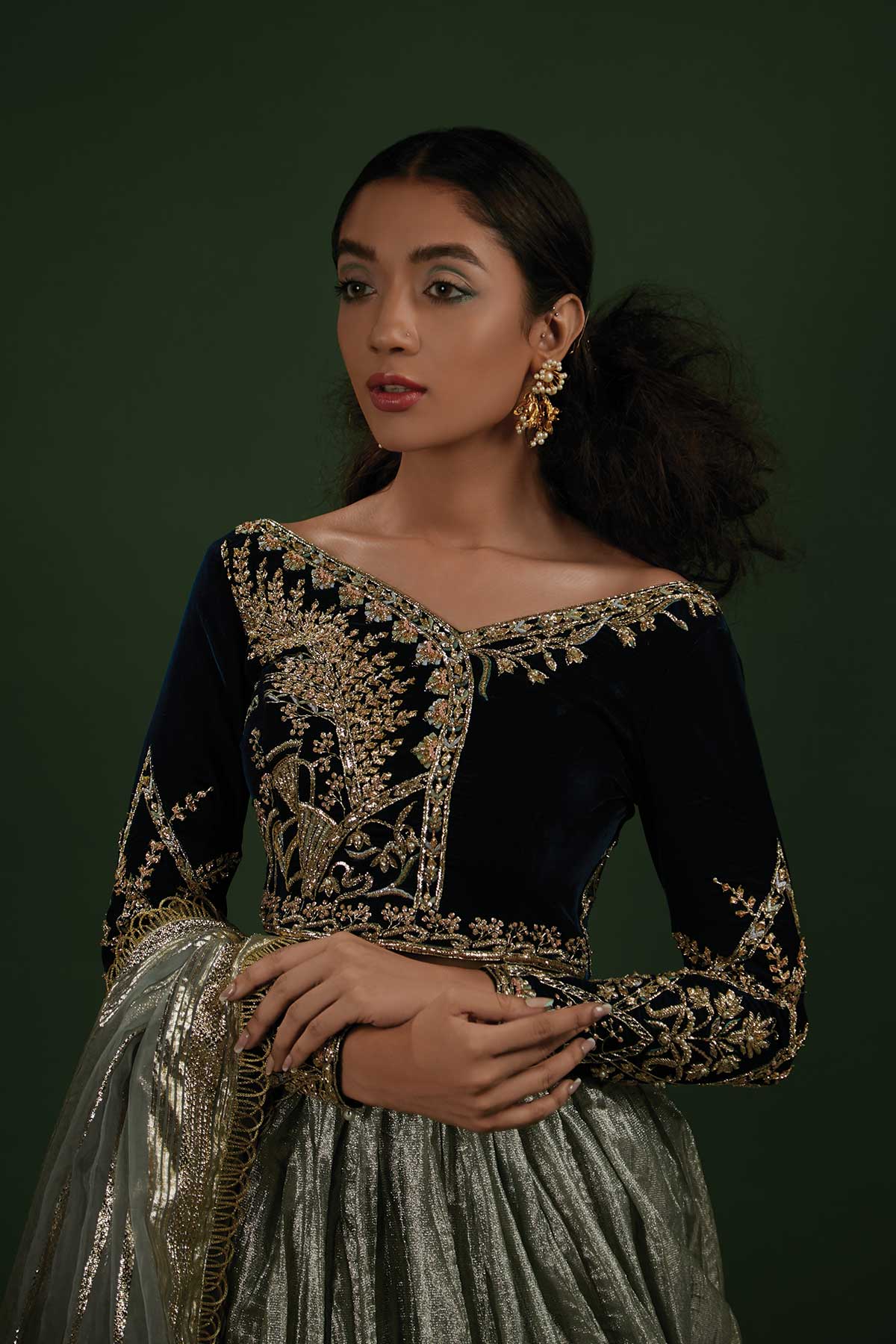 Model in a closeup shot wearing a formal teal velvet choli paired with a mint-ice blue crushed lehenga made of shimmered fabric and an organza zari dupatta