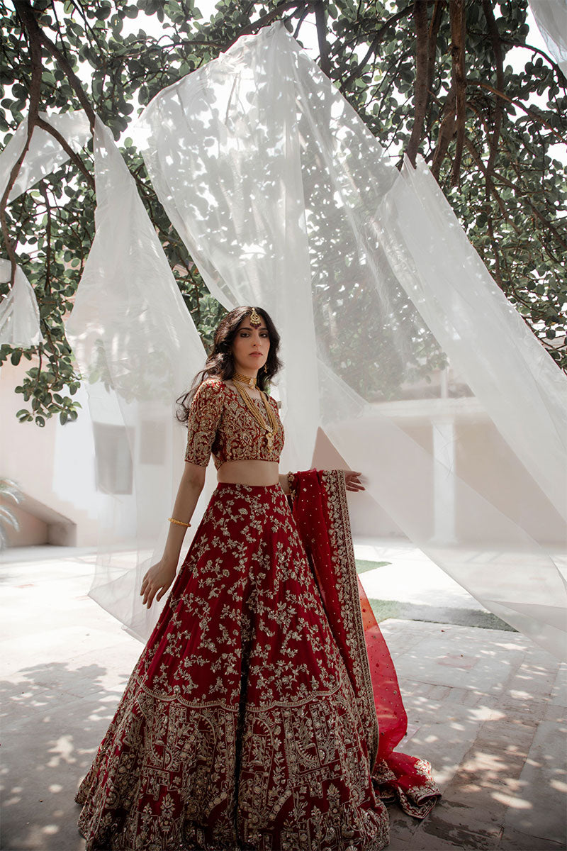 Model in a side shot wearing maroon raw silk bridal lehnega paired with organza dupatta and silk brocade choli