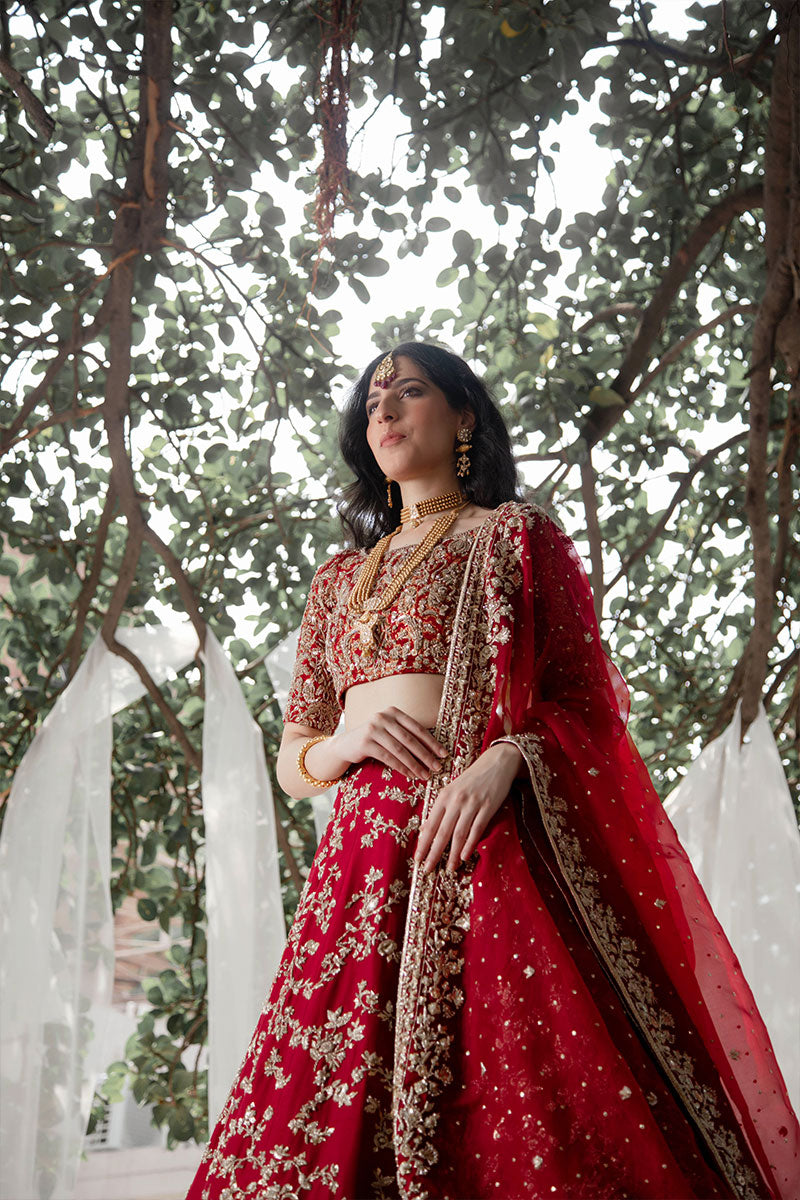 Model in a front view shot wearing maroon raw silk bridal lehnega paired with organza dupatta and silk brocade choli