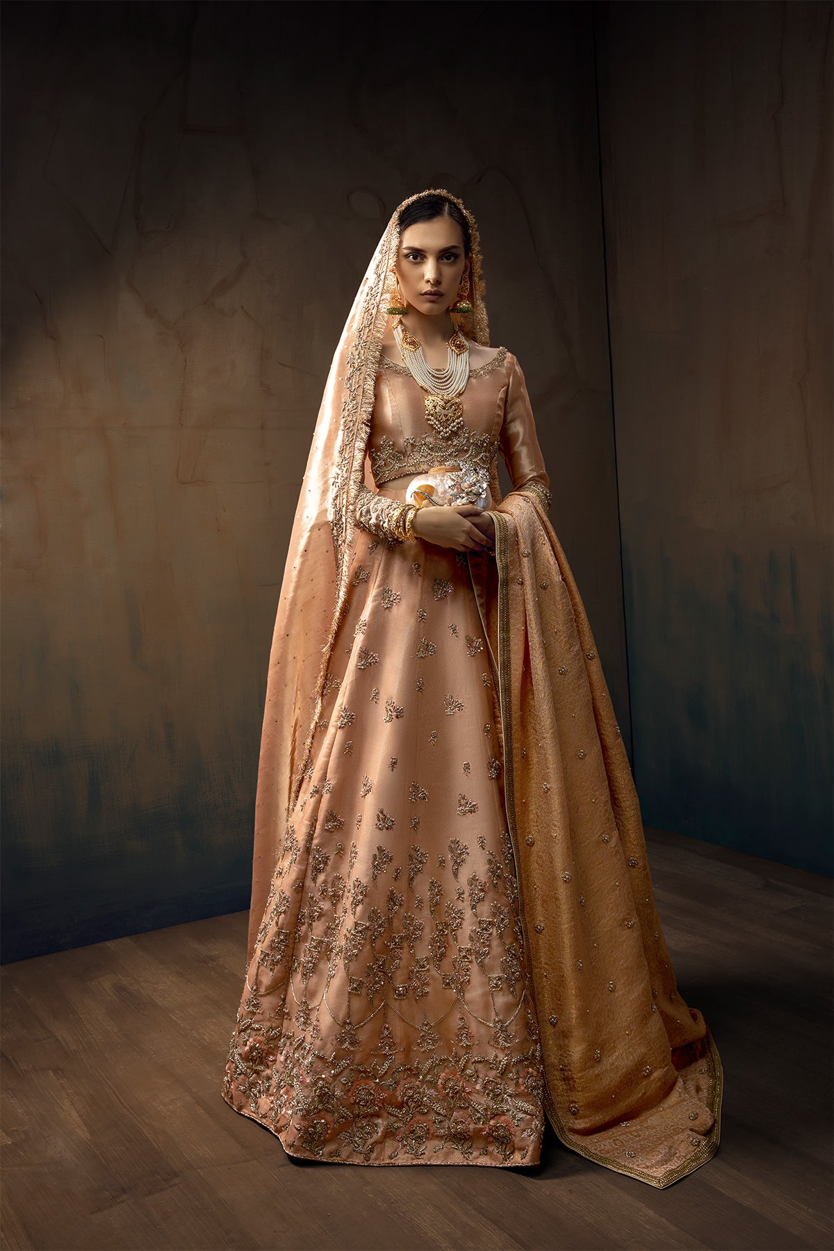 Model in a front full shot wearing melon pink lehenga in organza fabric paired with a pure tissue choli, dupatta accompanied by a jamavar shawl