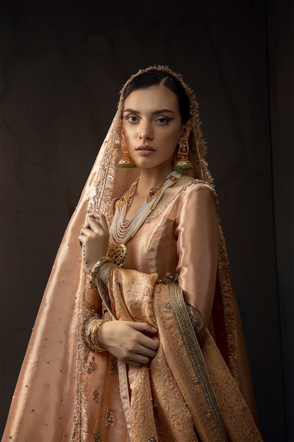 Model in a closeup shot wearing melon pink lehenga in organza fabric paired with a pure tissue choli, dupatta accompanied by a jamavar shawl