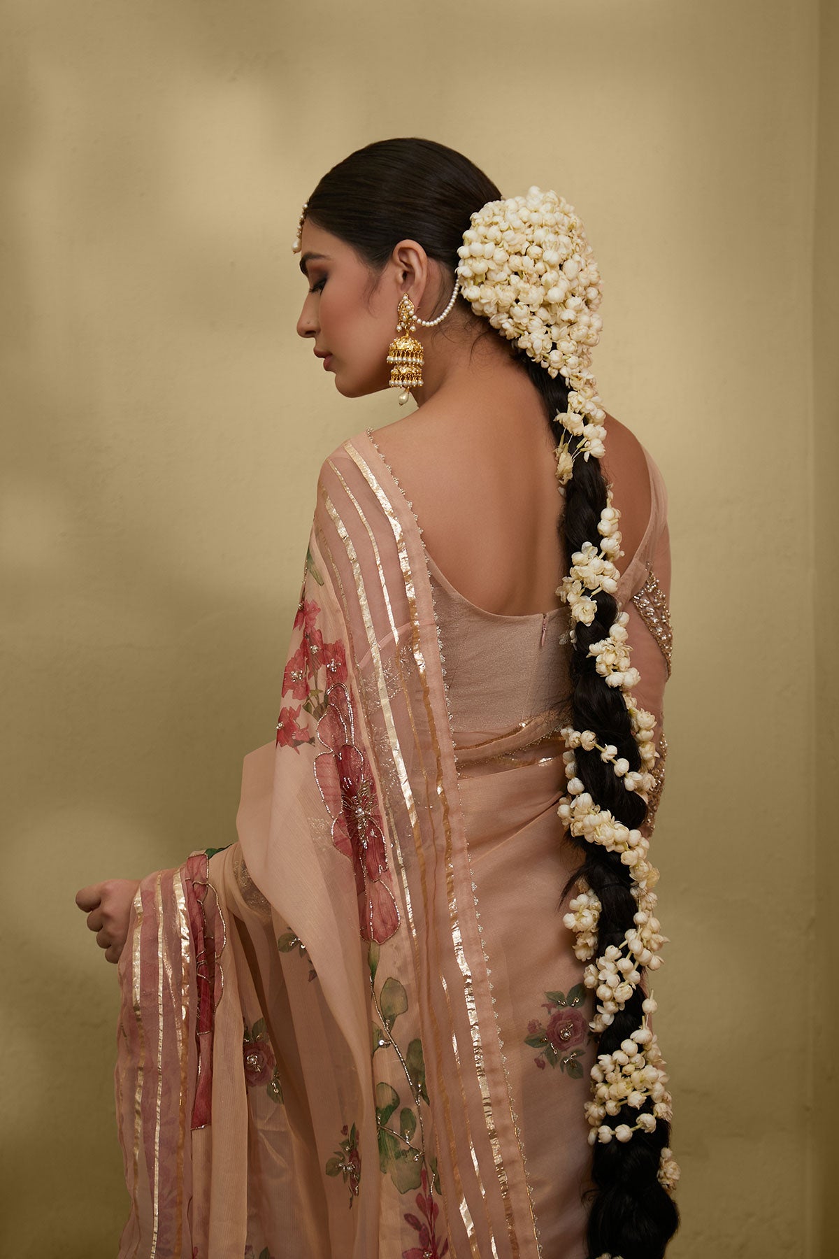 Model in a back closeup shot wearing pastel pink printed massouri saree with a two-tiered net gathering and is paired with a net blouse 