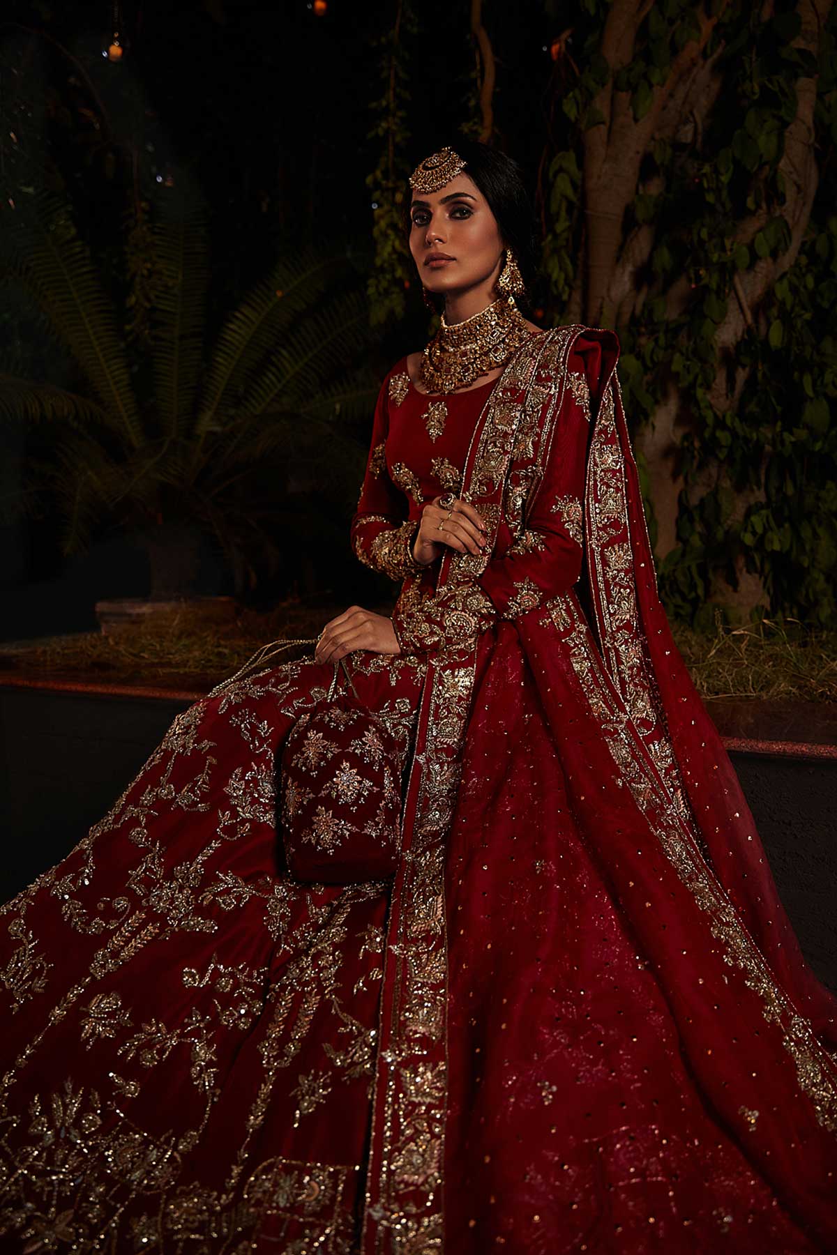 model in a seated side shot wearing red bridal lehenga choli in raw silk fabric paired with silk organza dupatta