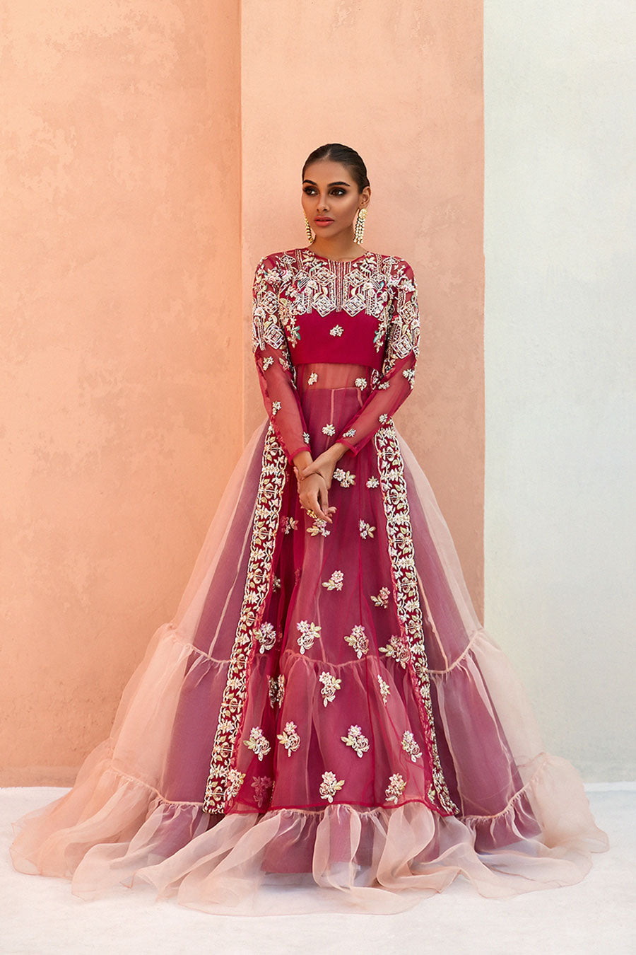 model in a front shot wearing formal rose pink net long slit shirt with sheer sleeves and silk bustier paired with a double-layered lehenga