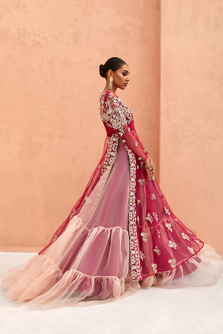 model in a side shot wearing formal rose pink net long slit shirt with sheer sleeves and silk bustier paired with a double-layered lehenga