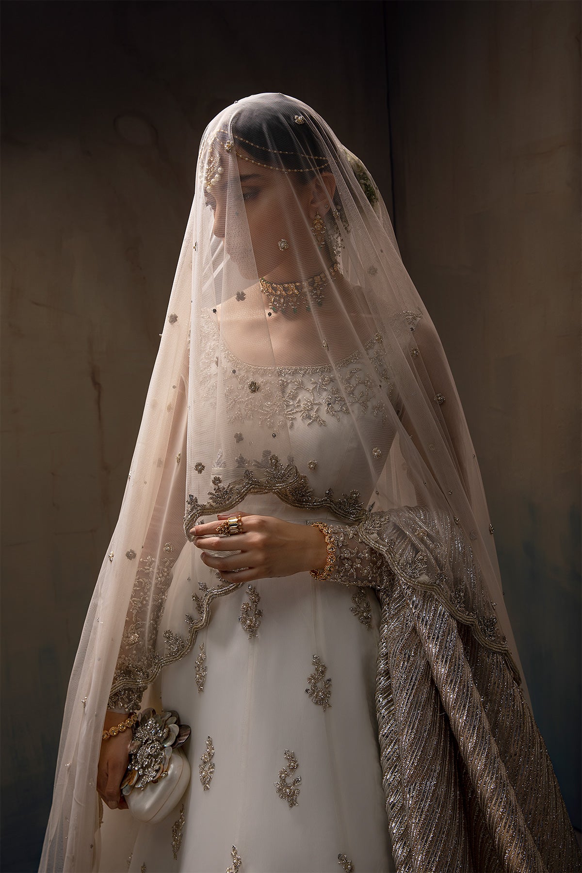 Model in a front half shot wearing white long pishwas gown paired with net dupatta along with a silver shawl 