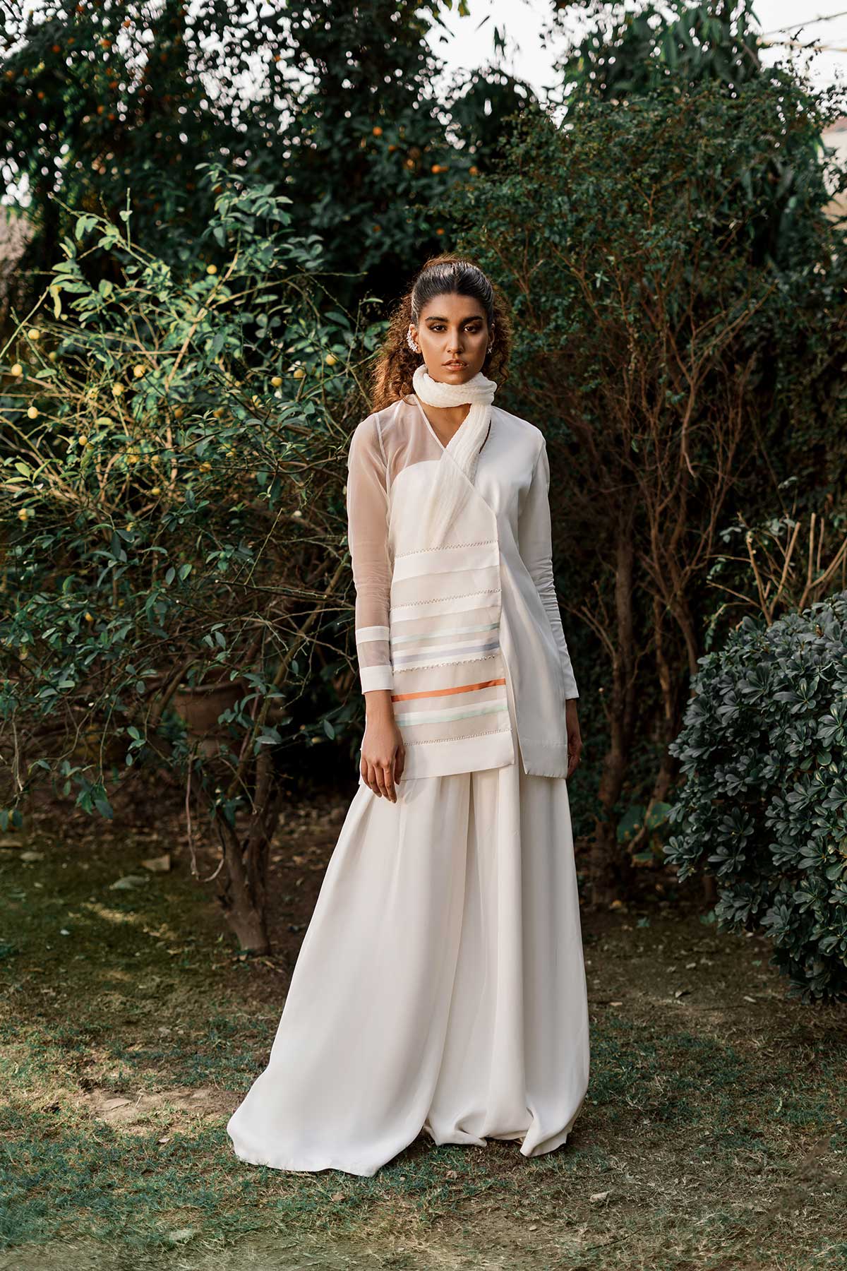 Model in a front shot wearing jacket with a sheer organza side paired paired with flared pants, a bustier, and a crushed dupatta